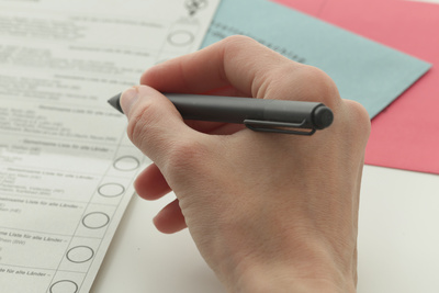 Hand mit Stift über Wahlzetteln